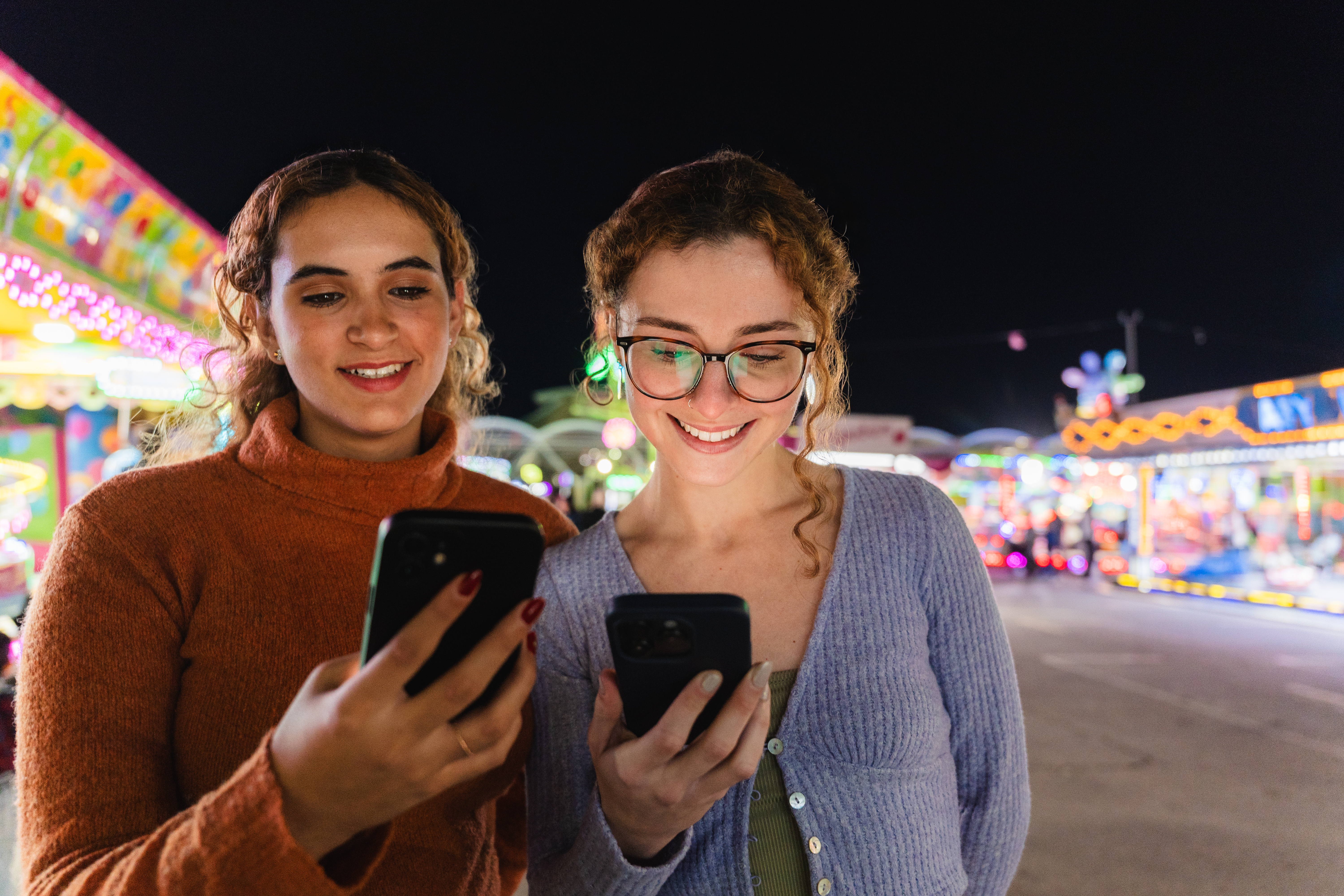 Two women playing Promo on Demand games on their cell phones at a fairground